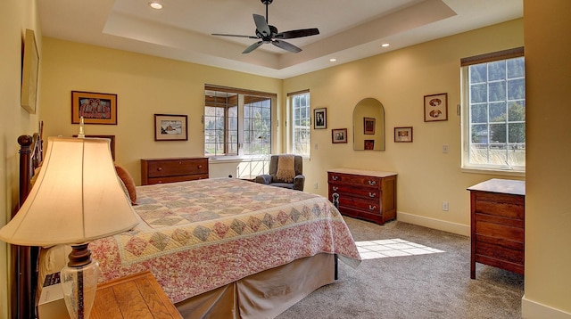 carpeted bedroom with ceiling fan and a raised ceiling