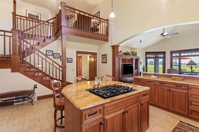 kitchen featuring ceiling fan, brown cabinetry, arched walkways, light tile patterned floors, and black gas stovetop