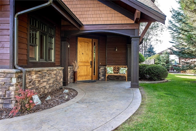 entrance to property with a shingled roof, a yard, and stone siding