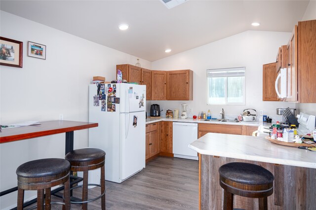 kitchen featuring hardwood / wood-style floors, white appliances, lofted ceiling, kitchen peninsula, and a breakfast bar