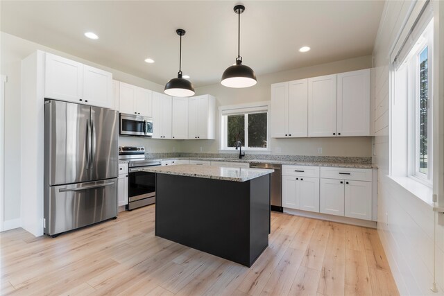 kitchen featuring white cabinets, light stone countertops, stainless steel appliances, light hardwood / wood-style floors, and a kitchen island