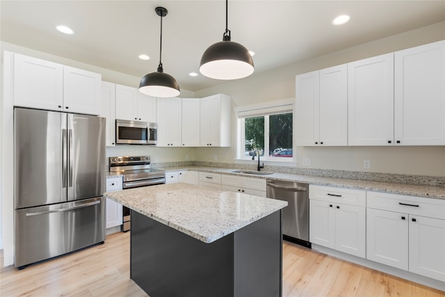 kitchen featuring a kitchen island, appliances with stainless steel finishes, light hardwood / wood-style floors, hanging light fixtures, and sink