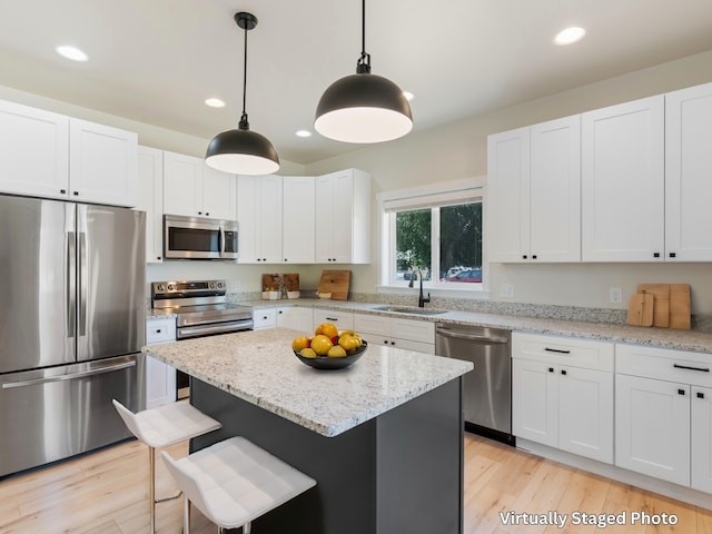 kitchen with appliances with stainless steel finishes, a kitchen island, pendant lighting, and white cabinetry