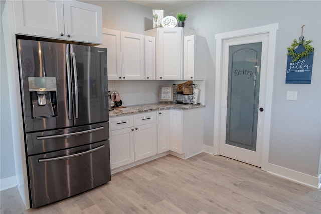 kitchen featuring light stone countertops, light hardwood / wood-style floors, white cabinetry, stainless steel fridge, and decorative backsplash