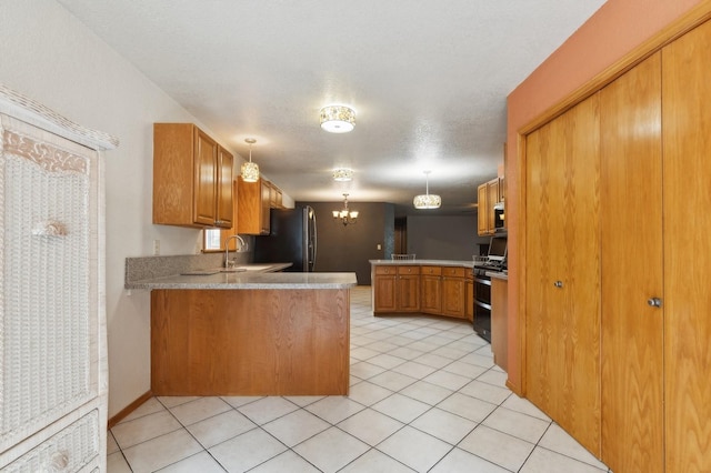 kitchen featuring brown cabinets, double oven range, freestanding refrigerator, a peninsula, and light tile patterned flooring