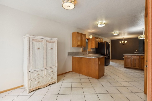 kitchen featuring brown cabinets, freestanding refrigerator, an inviting chandelier, a peninsula, and light tile patterned flooring