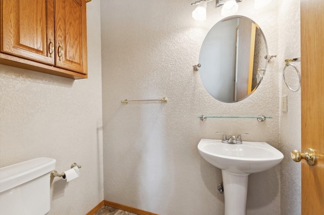 bathroom featuring toilet, a textured wall, and baseboards