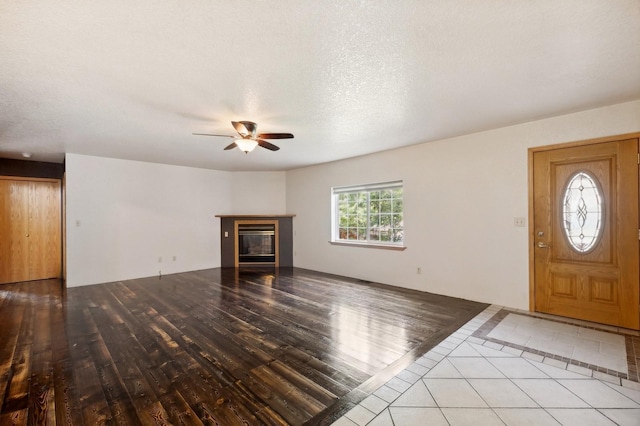 unfurnished living room featuring a glass covered fireplace, a ceiling fan, light wood-style floors, and a textured ceiling