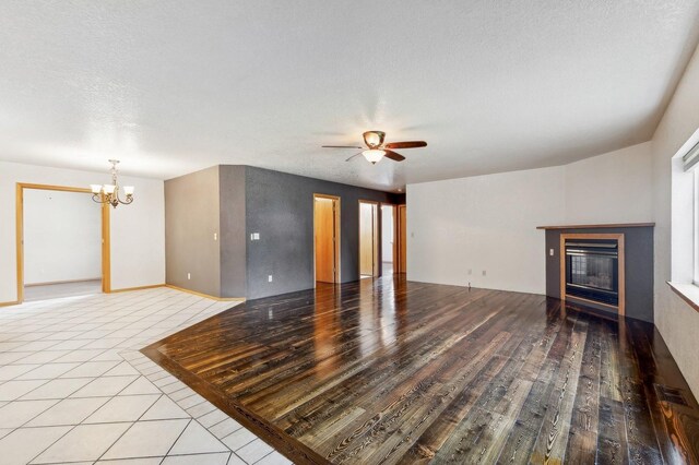 unfurnished living room with a textured ceiling and ceiling fan with notable chandelier