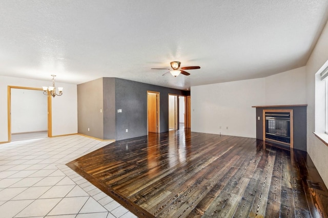 unfurnished living room featuring light wood finished floors, visible vents, ceiling fan with notable chandelier, a glass covered fireplace, and a textured ceiling