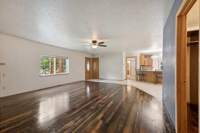 unfurnished living room with ceiling fan with notable chandelier, a textured ceiling, and hardwood / wood-style floors