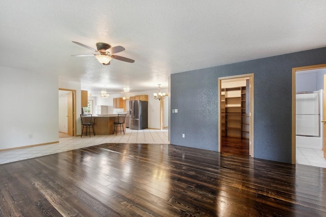 unfurnished living room featuring ceiling fan with notable chandelier, a textured ceiling, and hardwood / wood-style floors