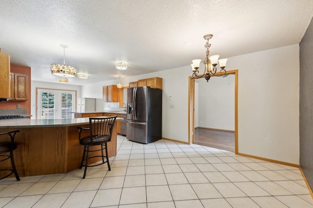 kitchen with a peninsula, french doors, a kitchen breakfast bar, a notable chandelier, and stainless steel fridge