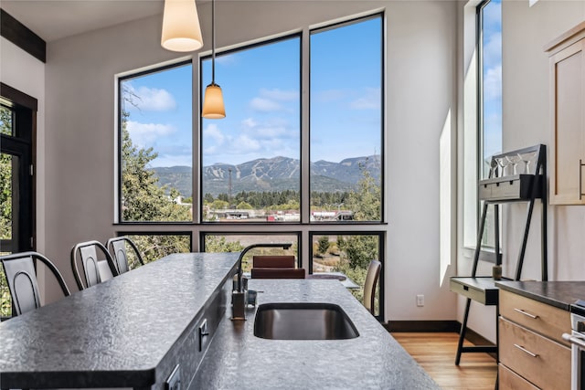 kitchen with sink, decorative light fixtures, an island with sink, light hardwood / wood-style flooring, and a mountain view