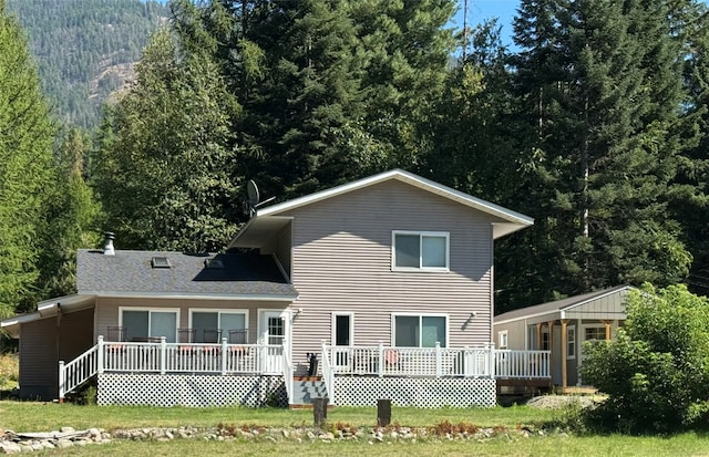 back of house featuring a wooded view, a lawn, and a wooden deck