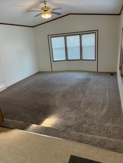 carpeted empty room with lofted ceiling, a ceiling fan, and ornamental molding