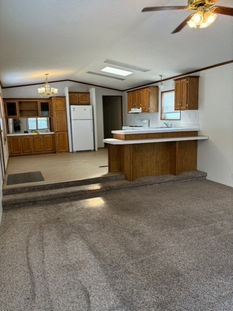 kitchen featuring a peninsula, freestanding refrigerator, light countertops, vaulted ceiling, and brown cabinets