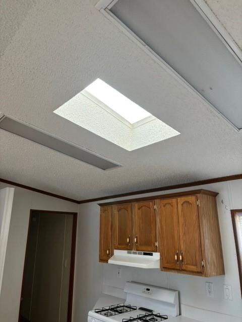 room details featuring white gas range oven, under cabinet range hood, a textured ceiling, crown molding, and brown cabinets