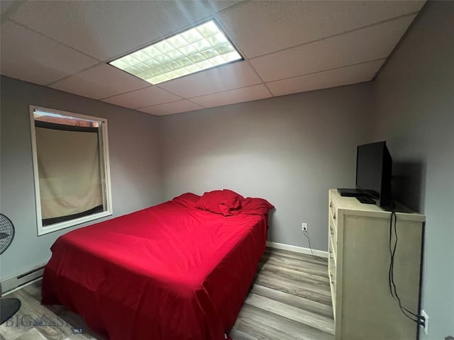 bedroom featuring light wood-type flooring, a paneled ceiling, and baseboard heating