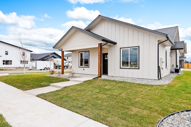 modern inspired farmhouse featuring a shingled roof, covered porch, central AC unit, board and batten siding, and a front lawn