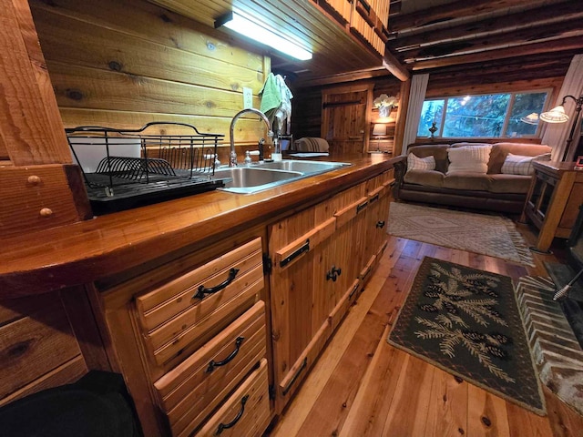 kitchen with light hardwood / wood-style flooring, wooden walls, butcher block counters, and sink