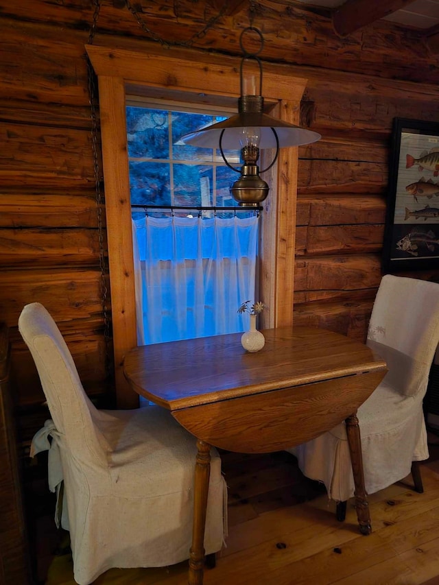 dining area with log walls, a notable chandelier, beamed ceiling, and hardwood / wood-style flooring