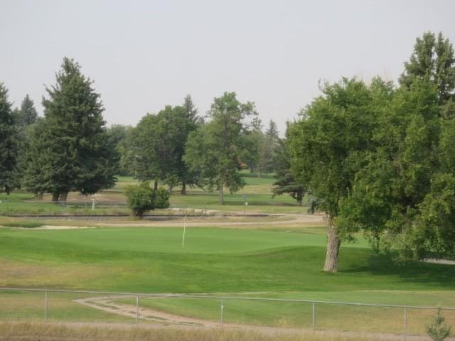 view of community with a yard, golf course view, and fence