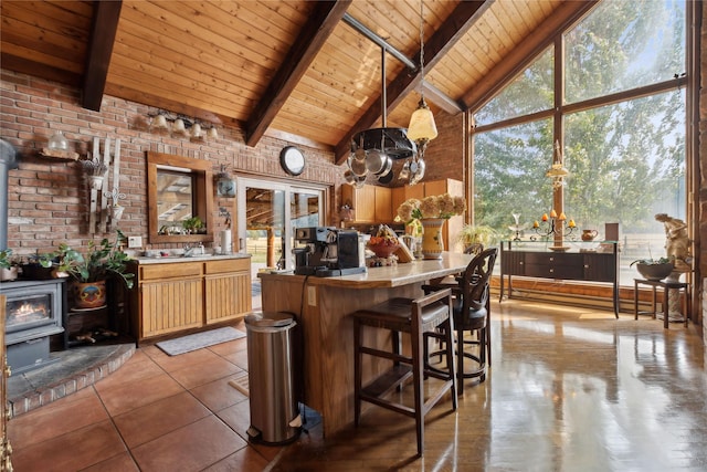 kitchen featuring beamed ceiling, wooden ceiling, brick wall, a chandelier, and a wood stove