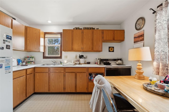 kitchen with a sink, range with electric stovetop, freestanding refrigerator, light countertops, and light floors