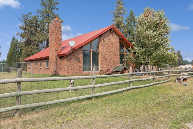 back of house with brick siding, fence, a lawn, a chimney, and metal roof