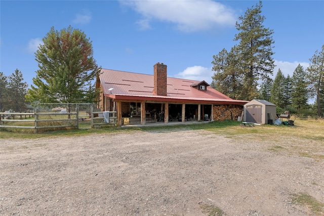 back of property featuring fence, a shed, a chimney, an outdoor structure, and metal roof