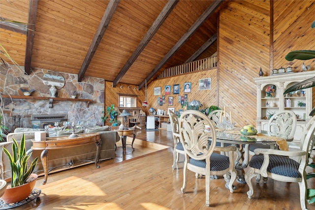 dining space with high vaulted ceiling, wood-type flooring, wooden walls, and a stone fireplace