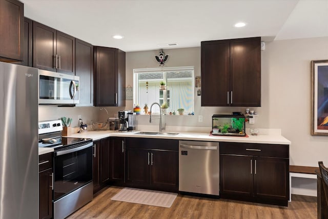 kitchen with dark brown cabinetry, a sink, light countertops, light wood-style floors, and stainless steel appliances
