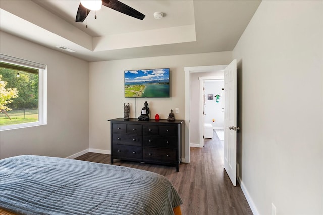 bedroom featuring ceiling fan, dark wood-style flooring, visible vents, baseboards, and a tray ceiling