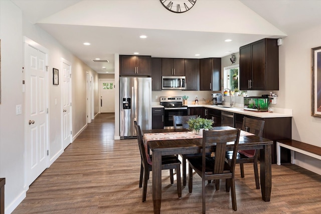 kitchen with a sink, appliances with stainless steel finishes, wood finished floors, and dark brown cabinets