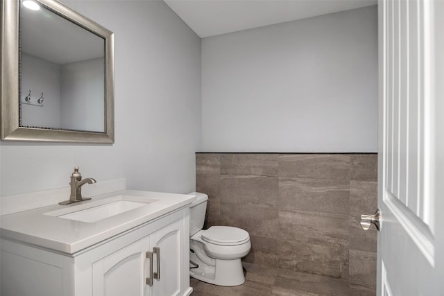 bathroom with vanity, tile walls, toilet, and a wainscoted wall