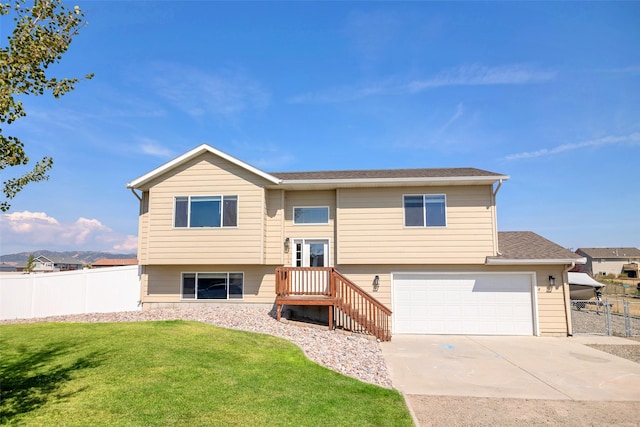 split foyer home with fence, roof with shingles, an attached garage, a front lawn, and concrete driveway