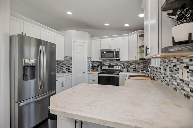 kitchen featuring vaulted ceiling, a peninsula, stainless steel appliances, white cabinetry, and a sink