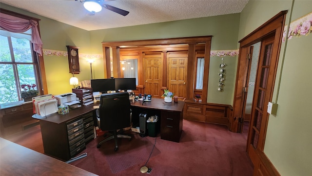 carpeted office space featuring ceiling fan, decorative columns, and a textured ceiling