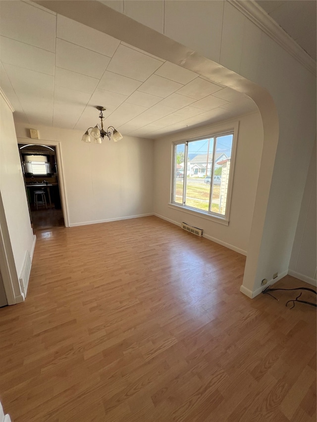 spare room featuring wood-type flooring, an inviting chandelier, and crown molding