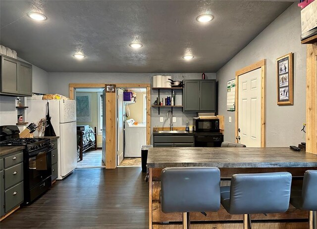 kitchen featuring dark wood-type flooring, a breakfast bar area, black appliances, washer / dryer, and sink