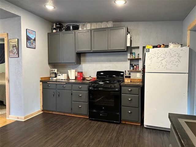 kitchen featuring white refrigerator, black range with gas stovetop, dark wood-type flooring, and gray cabinetry