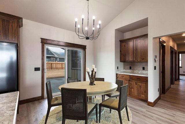 dining area featuring a chandelier, lofted ceiling, light wood-style flooring, and baseboards