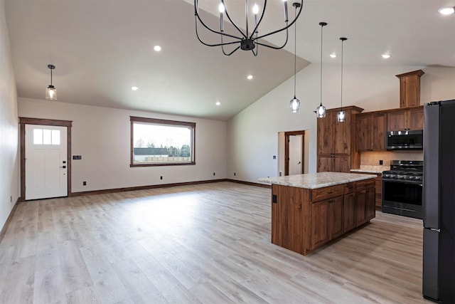 kitchen featuring light wood-type flooring, black range with gas stovetop, stainless steel microwave, and freestanding refrigerator