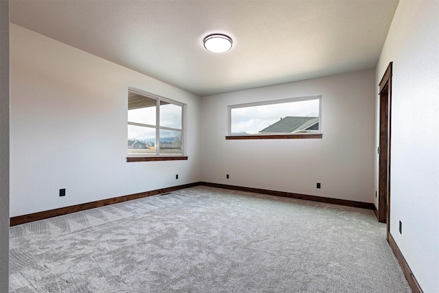 carpeted spare room featuring baseboards and a textured ceiling