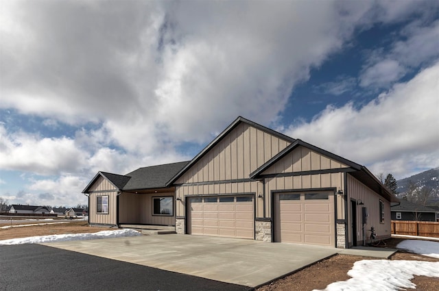 modern farmhouse style home featuring a garage, a shingled roof, concrete driveway, stone siding, and board and batten siding