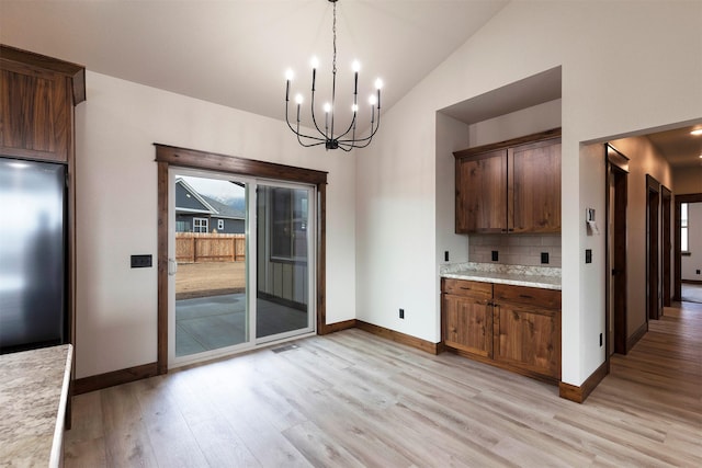 kitchen with lofted ceiling, light wood-style flooring, decorative backsplash, freestanding refrigerator, and baseboards