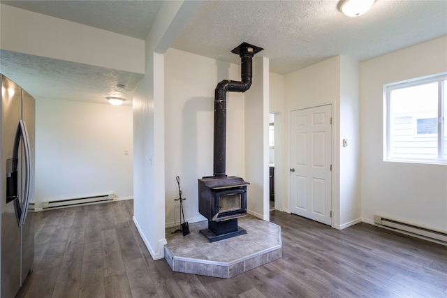 interior space with a textured ceiling, hardwood / wood-style flooring, a baseboard radiator, and a wood stove