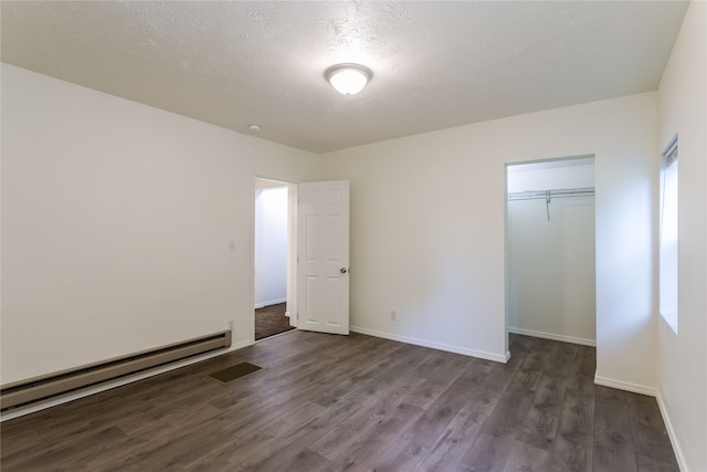 unfurnished bedroom with a textured ceiling, baseboard heating, dark hardwood / wood-style floors, and a closet