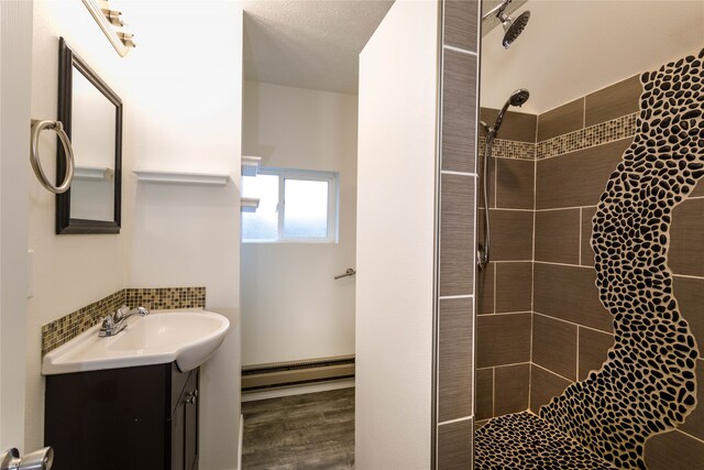 bathroom with a baseboard radiator, a tile shower, wood-type flooring, and vanity